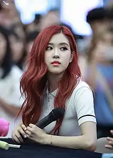 Rosé sits at a table holding a microphone, looking sideways.