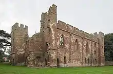 A ruined building minus a roof and with crumbling walls. Some of the walls are crenelated. The walls are build with red stones in the middle and grey stones as edging on the tops and corners