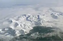  Aerial view of a range of icy mountains with a coastline visible in the foreground