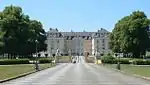 A giant stretch of road leads to an open gate enclosing a large palace.