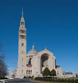 Tree-lined entry road leading to the main façade, showing the entry with the great rose window, dome, and bell tower attached to the left of the main structure