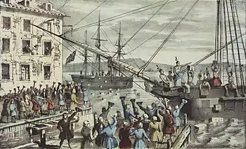 Two ships in a harbor, one in the distance. On board, men stripped to the waist and wearing feathers in their hair throw crates of tea overboard. A large crowd, mostly men, stands on the dock, waving hats and cheering. A few people wave their hats from windows in a nearby building.