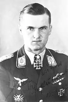 The head and shoulders of a young man, shown in semi-profile. He wears a military uniform with an Iron Cross displayed at the front of his shirt collar.