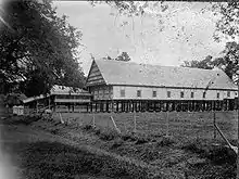 A black and white picture of a thatched roof building on stilts