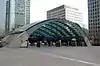 A wide, grey archway with a blue sign reading "CANARY WHARF STATION" in white letters and a man in a black suit walking through