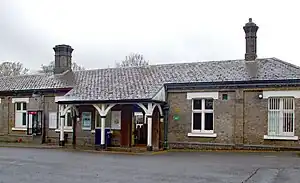 A brown-bricked building with two brown-bricked chimneys, some trees in the background, and a speed bump in the foreground all under a blue sky