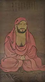 A seated monk in a red robe.