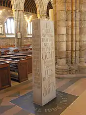 a cuboid-shaped standing stone with words engraved on its sides and on the floor where it stands.