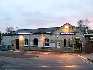 A white- and beige-bricked building with a blue sign reading "FINCHLEY CENTRAL STATION" in white letters all under a blue sky fading to purple on the horizon