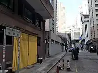 北角清華街的路牌及向東面的街景，可見遠處有一條斜路通往白色外牆的蘇浙小學，在斜路左邊的清華街19號有一幢三層高的建築物，於1960至1970年代是聖猶達小學，小學於1980年被關閉後原址改為開辦幼稚園，圖中近中央的遠處可見在通往蘇浙小學的斜路側邊，與原址是聖猶達小學之間有一段掘頭路，並有私家車停泊，案中的兩名兒童便是在斜路下的該段路面被炸死，圖中右側有一輛車牌LV3821的黑色私家車背向停泊於一幢住宅大廈外面的圍欄柱之間，黃姓小姊弟在1967年被炸死時便是居於該處的清華街20號，該處於1980年代重建為現時的多層公寓富景閣（攝於2021年2月）