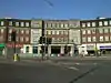 A brown-bricked building with white columns and a sign reading "HENDON CENTRAL STATION" in blue letters all under a clear, blue sky