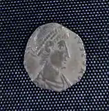 A small silver coin mostly consisting of a human head and shoulders. The shape is irregular and there is only a vestige of writing.