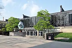  a low steel and glass building and concrete courtyard, with the words Paul V. Galvin Library about a bank of doors, flanked by trees and an abstract steel sculpture