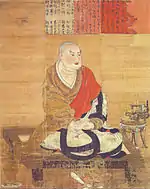 Priest seated cross-legged on a pedestal.