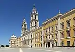 A massive building with yellow facade and two bell towers in the middle