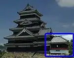 A one-storied structure with a veranda with red handrail connected to a two-storied castle tower. Both are located on a platform of unhewn stones.