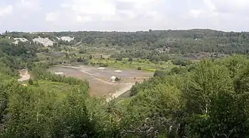 An open quarry pit in the middle of rolling, shrub covered hills