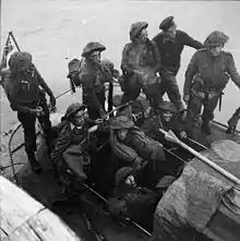 nine British soldiers and one sailor on a small boat at sea. A union Jack flies from a mast at the rear