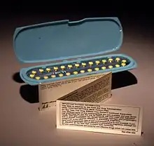 An oblong blue container holding 28 yellow pills, with a small, folded paper note standing in front of it