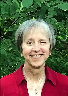 Head of woman in her sixties smiling in an outdoor natural setting.