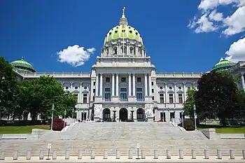 Looking up from a large, stone staircase is a marble facade of a building with a large, pale green dome. Several people are walking down the stairs.