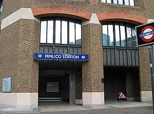 A brown-bricked building with a rectangular, dark blue sign reading "PIMLICO STATION" in white letters and a black sign reading "UNDERGROUND"