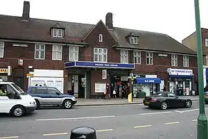 A red-bricked building with a rectangular, dark blue sign reading "PRESTON ROAD STATION" in white letters all under a clear, white sky