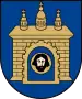 A coat of arms depicting a grey castle with three towers topped by crosses with a human head on the front door all on a blue background