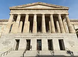 A 3 story building. The first story is granite, while the second two are sandstone. There is a pedimented front with columns spanning the second and third floors and the entrance on the first.