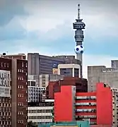 A concrete tower, the bottom obscured by other buildings, viewed from below. A large football shaped structure has been fitted to the tower just below the habitable section.