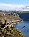 A river winds between high cliffs and hills, with a castle in the midground.