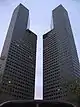 Ground-level view of two identical 45-storey towers with rectangular cross sections; a diagonal cut-out is present on each tower near the 30th floor