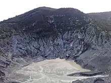 A photograph depicting a white sky at the top, a grey land configuration in the middle, and a body of water swirling around at the bottom.