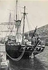  A ship with three masts and a tall central funnel, tied to the dockside with loose ropes so that the stern is swinging outwards