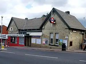 A beige-bricked building with a rectangular, dark blue sign reading "TOTTERIDGE & WHETSTONE STATION" in white letters all under a blue sky