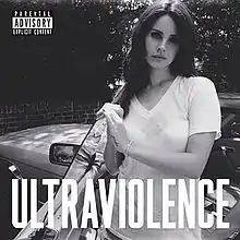 A black and white photo of a fair-skinned, dark-haired woman wearing a sheer white V-neck T-Shirt and a white strapless bra, standing beside a car. Her hand is resting on the opened left car door and the word "Ultraviolence", stylized in all capital letters, is placed on the lower part of the picture.