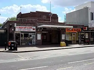 A red-bricked building with a rectangular, dark blue sign reading "UPMINSTER BRIDGE STATION" in white letters all under a blue sky