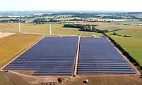 Aerial view of a solar farm with part of a wind farm in the background